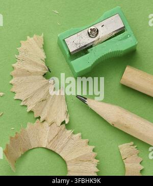 Grüner Kunststoff-Bleistiftspitzer, scharfer Holzbleistift und profilierte Späne auf grünem Hintergrund, Draufsicht, Vorbereitung für das Zeichenkonzept Stockfoto
