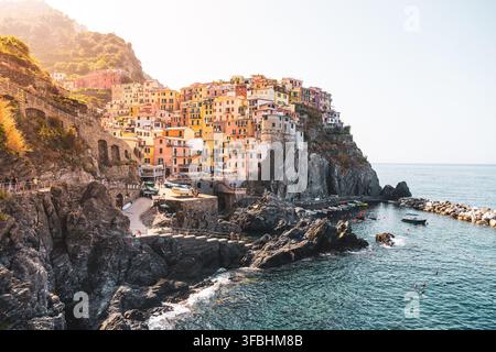 Farbenfrohe Häuser sitzen auf den Klippen mit Blick auf das Meer im Dorf Manarola. Menschen genießen das Wasser und die Aussicht an einem sonnigen Tag in dieser Küstenregion Italiens. Stockfoto