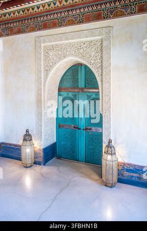 Das Bild zeigt eine dekorative blaue Tür im Turm des Geheimen Gartens in Marrakesch, Marokko. Die Tür weist aufwendige Designelemente auf und wird von Laternen flankiert. Stockfoto