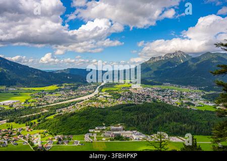 Reutte wird von hoch oben auf einem Berg aus gesehen. Die Stadt ist von grünen Feldern und Bäumen umgeben. Ein Fluss fließt durch das Gebiet unter einem blauen Himmel mit Wolken. Stockfoto