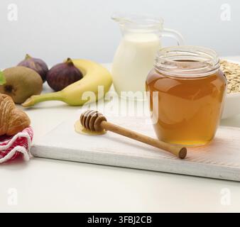 Honig in einem durchsichtigen Glas aus Glas und ein Holzstab auf einem weißen Tisch Stockfoto