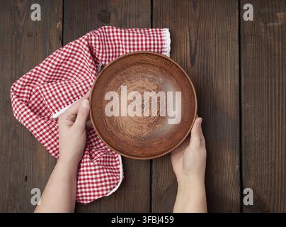 Zwei weibliche Hände halten eine leere runde Ton Platte, Ansicht von oben Stockfoto