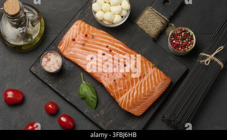Zusammensetzung aus frischen Zutaten Lachsstück, Kirschtomaten, Mozzarella-Kugeln und schwarzen Nudeln. Schwarzer Tisch, Draufsicht Stockfoto
