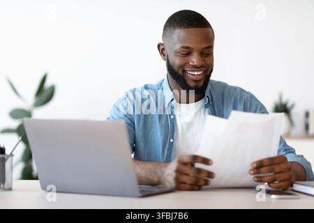 Fröhlicher Junger Schwarzer Unternehmer, Der Mit Papieren Im Modernen Büro Arbeitet Stockfoto