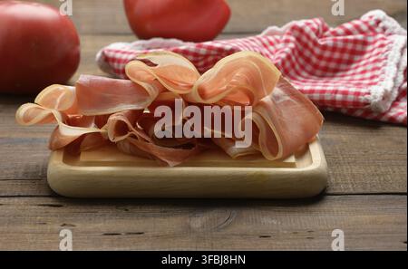 In Scheiben geschnittene dünne Scheiben Schinken auf braunem Holzbrett, Holztisch Hintergrund Stockfoto
