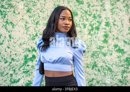 Junge schwarze Frau trägt ein trendiges Crop Top und einen Rock vor einer strukturierten grünen Wand Stockfoto