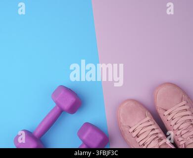 Paar Turnschuhe aus rosafarbenem Leder, Kunststoff-Hanteln für Sport auf pinkblauem Hintergrund, Sportkulisse, Draufsicht, Kopierraum Stockfoto