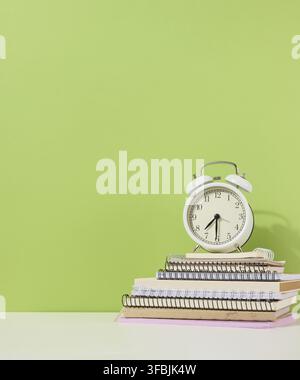 Rund-Wecker steht auf einem Stapel Notizbücher, grüner Hintergrund. Zurück in die Schule Stockfoto