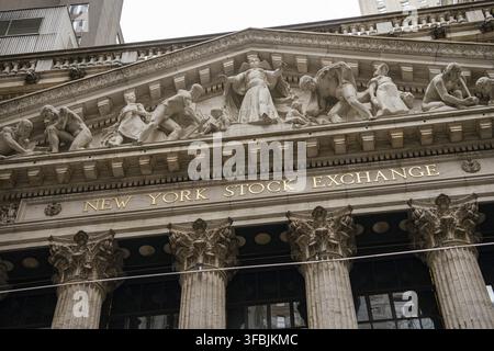 Nahaufnahme des Schildes der New York Stock Exchange unter seinem gestalteten Giebel an der Wall Street. Klassische Steinrelieffiguren repräsentieren Handel und Ind Stockfoto