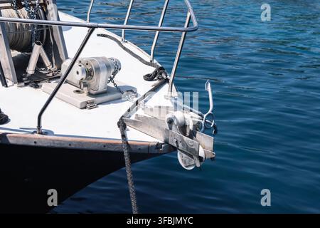Nahaufnahme des Bug eines weißen Bootes mit Metallgeländer, Windenmechanismus, schwerem Anker und Seilen, die auf der ruhigen blauen Meeresoberfläche in Gree schwimmen Stockfoto