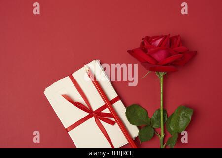 Rote blühende Rose, ein Stapel von Vintage-Papierkarten und roter Holzstift auf einem farbigen Hintergrund, Draufsicht Stockfoto