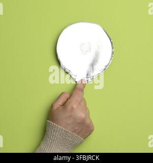 Runder dünner Deckel aus Aluminium für Joghurtgläser aus Kunststoff auf grünem Hintergrund, Nahaufnahme Stockfoto