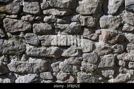 Eine Nahaufnahme einer Wand aus großen, unebenen Steinen. Die Textur der Steine ist rau, mit unterschiedlichen Schattierungen von Grau und Braun Stockfoto