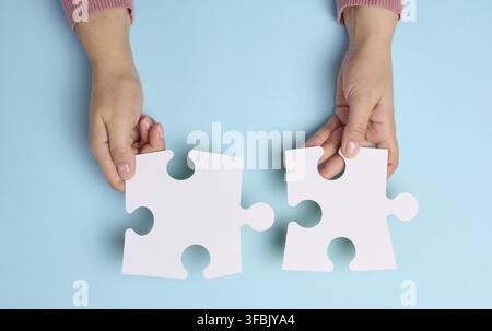Weibliche Hand hält zwei große leere weiße Puzzles auf blauem Hintergrund, Draufsicht Stockfoto