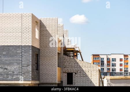 Seitenansicht einer modernen mehrstöckigen Backsteinfassade im Bau neben einem fertiggestellten Wohnkomplex im Freien an einem hellen sonnigen Sommertag Stockfoto