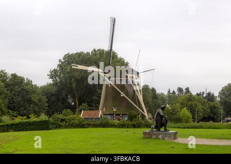 Ansicht der De Riekermolen, einer historischen Windmühle aus dem 17. Jahrhundert, eingebettet in einen üppigen grünen Park mit einer Statue von Rembrandt im Vordergrund unter einem bewölkten Himmel Stockfoto