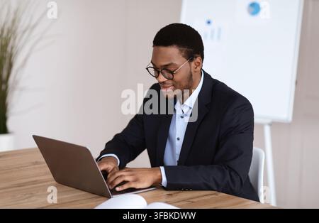 Junge schwarze Manager lächeln während der Arbeit mit Laptop, Büroeinrichtung Stockfoto