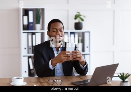Junger afrikanischer Mann im Anzug mit Smartphone im Büro Stockfoto