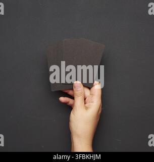 Weibliche Hand mit einem Stapel leerer schwarzer Visitenkarten Vor dem Hintergrund einer leeren schwarzen Kreidetafel Stockfoto