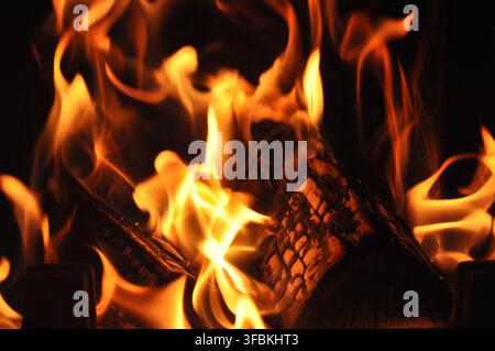 Nahaufnahme von brennendem Brennholz mit hellen orangefarbenen Flammen vor dunklem Hintergrund. Stockfoto