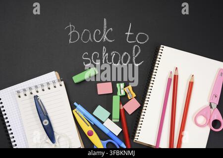 Schulbedarf: Mehrfarbige Holzstifte, Notizbuch, Bleistiftspitzer und weiße Kreideeinschrift zurück zur Schule auf schwarzem Hintergrund, Hintergrund Stockfoto