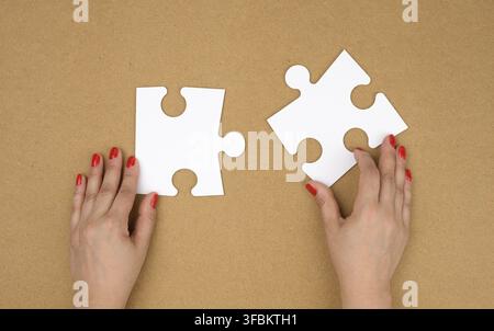Zwei leere papierweiße Puzzleteile in weiblichen Händen, Puzzle verbunden, brauner Hintergrund, Draufsicht Stockfoto