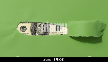 Ein grünes Blatt Papier mit einem zerrissenen Mittelteil und einem gekräuselten Rand, ein Hundert-Dollar-Schein im Loch Stockfoto