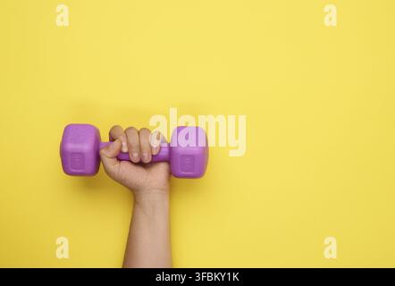 Weibliche Hand hält eine lila ein Kilogramm Hantel auf einem gelben Hintergrund, Copy Space Stockfoto