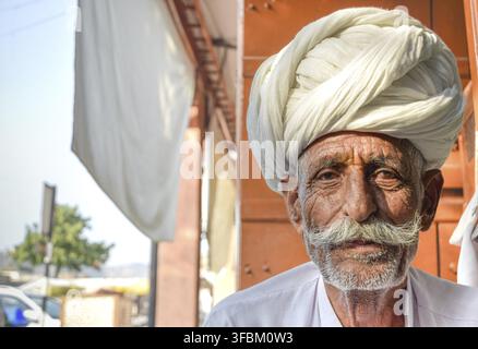 Älterer Mann mit traditionellem Rajasthani-Turban posiert vor der Kamera mit warmen Orangetönen im Hintergrund Stockfoto