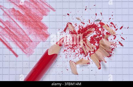 Roter Bleistift auf einem Blatt Notizbuch mit gezeichneten Strichen, roter Bleistiftspäne. Draufsicht Stockfoto