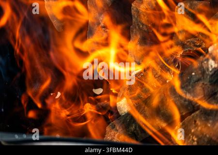 Makroaufnahme von lebhaften orangefarbenen und gelben Feuerflammen, die über brennenden Holz Kohlen in einem Außengrill ohne Menschen bei Tageslicht wirbeln. Stockfoto