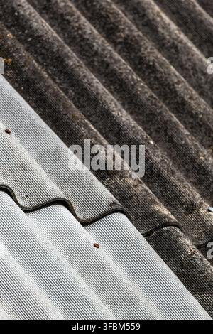 Nahaufnahme einer vertikalen Aufnahme, die die wellige Textur und das Muster alter welliger Asbestdachplatten aus Schiefer zeigen, mit hellgrauen und dunkel verwitterten Abschnitten Stockfoto