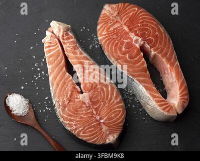 Zwei rohe Lachssteaks mit weißem Salz auf schwarzem Hintergrund, Draufsicht Stockfoto