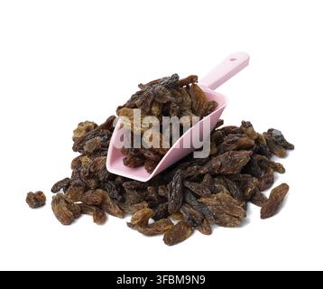Ein Haufen getrockneter brauner Rosinen in einem pinken Plastiklöffel auf weißem Grund Stockfoto