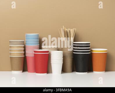 Stapel von verschiedenen Einweg-Pappbechern für Getränke, Kaffee und Tee auf einem weißen Tisch. Getränkebehälter zum Mitnehmen Stockfoto
