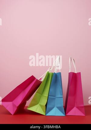 Vier leere, bunte Papiertaschen zum Einkaufen und Geschenke mit weißen Griffen stehen auf einem pink-roten Hintergrund, Kopierraum Stockfoto