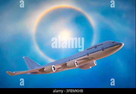 Generisches Modell eines Verkehrsflugzeugs, das vor einem auf einem Bildschirm angezeigten Hintergrund eines Sonnenhalo-Phänomens in einem blauen Himmel schwebt Stockfoto