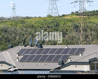 Ansicht von Solarmodulen, die auf einem Ziegeldach montiert sind, mit Satellitenschüsseln und Hochspannungsleitungen im Hintergrund in Sariyer, Istanbul, Türkei. Stockfoto