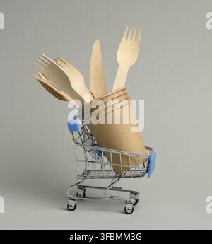 Einweg-Braune Pappbecher und Holzgabeln in einem Miniatur-Einkaufswagen aus Eisen auf grauem Hintergrund. Zero Waste Stockfoto