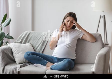Schwangere Frau Fühlt Sich Unwohl, Während Sie Zu Hause Auf Dem Handy Spricht Und Kopfschmerzen Hat Stockfoto