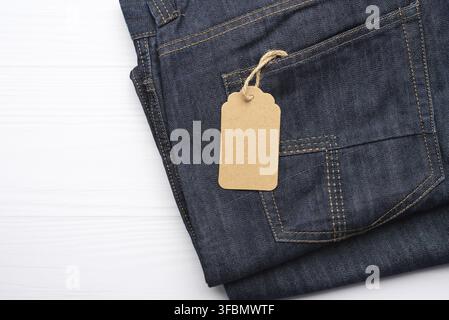 Blank braun rechteckigen Tag in der hinteren Tasche der blauen gefalteten Jeans auf weißem Hintergrund gebunden, Draufsicht Stockfoto