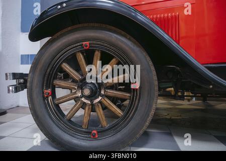 Detaillierte Nahaufnahme erfasst das Vorderrad eines klassischen roten Autos. Das Rad verfügt über Holzspeichen, schwarze Felge und Schrauben mit roter Kappe, die Handwerkskunst zeigen Stockfoto