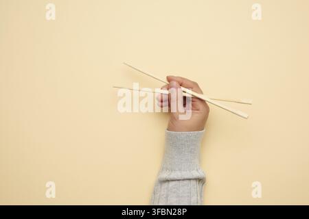 Paar Holzstäbchen in weiblicher Hand auf beigem Hintergrund, Nahaufnahme Stockfoto