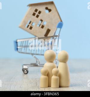 Holzhaus und Miniaturfiguren einer Familie auf blauem Hintergrund. Das Konzept des Verkaufs und Kaufs von Immobilien, Investitionen Stockfoto