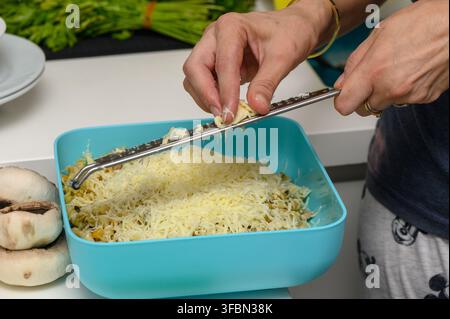Female chef reibt Käse über dampfende Pasta in einer hellen Küche und schafft eine warme und appetitliche Atmosphäre für ein hausgemachtes Gericht. Stockfoto