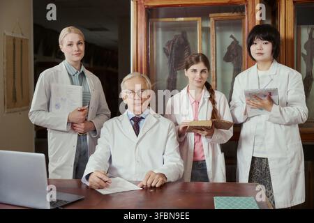 Porträt eines älteren kaukasischen Professors und vielfältiger junger erwachsener Studentinnen, die in einem Wissenschaftslabor posieren. Bild repräsentiert akademische Mentorschaft, geeignet für Universitätsmarketing Stockfoto