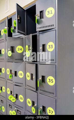 Dunkelgraues Metallschranksystem mit gelben runden Etiketten und eingelegten Schlüsseltaganhängern an offenen Türen. Konzept für sichere Lagerlösungen, Fitnessstudio-Umkleideräume, a Stockfoto