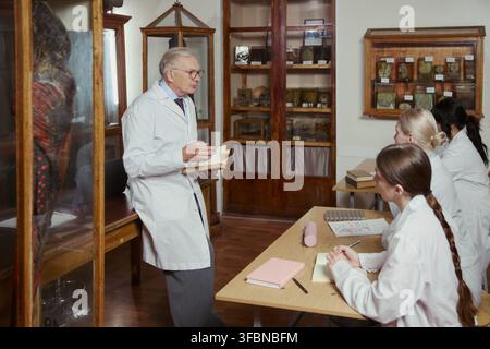 Seniorer kaukasischer Professor hält eine Vorlesung für junge erwachsene Medizinstudentinnen in einem Anatomiemuseum. Bild repräsentiert Hochschulbildung und eignet sich für universitäre Werbematerialien Stockfoto