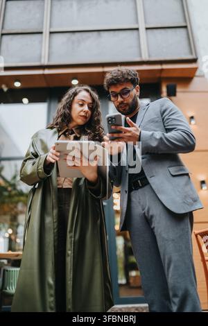 Geschäftskollegen überprüfen Tablet und Smartphone gemeinsam vor einem modernen Bürogebäude Stockfoto