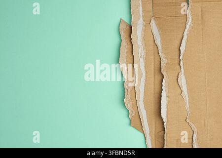 Zerrissene Kanten von welligem braunem Kartonpapier auf einem grünen Hintergrund. Schichten übereinander gestapelt, Platz für eine Inschrift Stockfoto